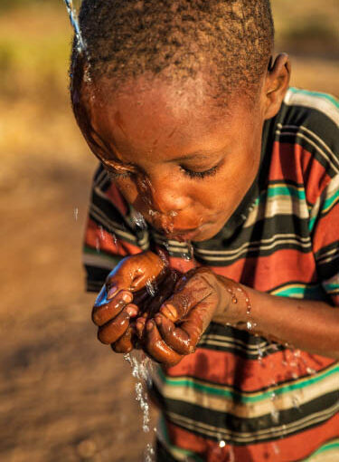 African child wearing tshirt drink water from cupped hands